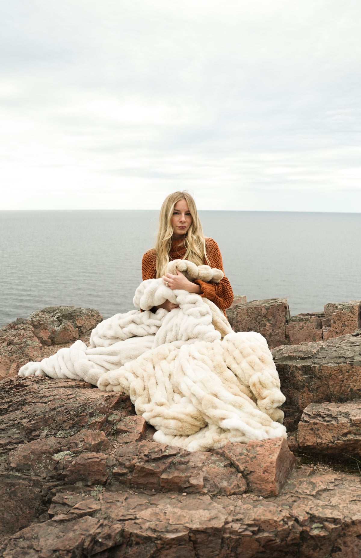 Cream faux fur blanket throw with layered marbled folds, draped on rocks